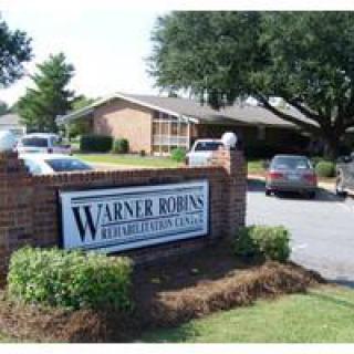 Entrance sign for Warner Robins Rehabilitation Center with building and parking area in the background.