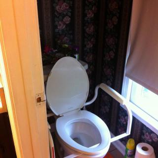 A bathroom with a toilet equipped with handrails for accessibility next to a window.