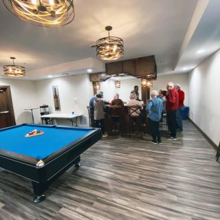 A group of people socializing in a game room with a pool table and bar area.