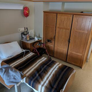 A view of a hospital patient room featuring a bed with a striped blanket and a wooden wardrobe.