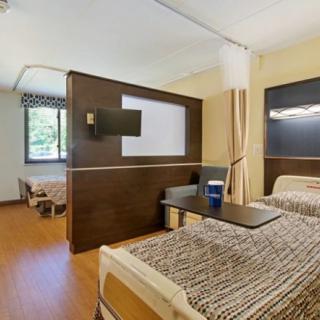 A modern hospital room with patient beds and a privacy curtain, featuring a television for comfort.