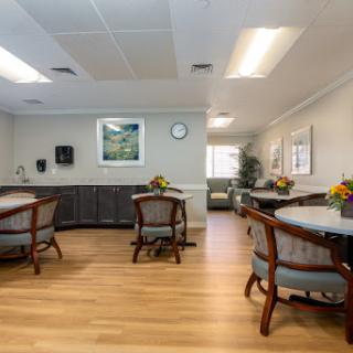 A spacious dining area in a healthcare facility, featuring wooden floors and comfortable seating.