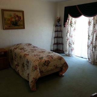 A cozy bedroom featuring a single bed with floral bedding, a nightstand, decorative curtains, and a framed painting on the wall.