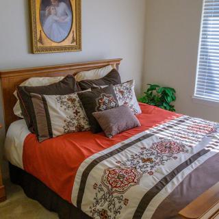 A cozy bedroom with a neatly made bed featuring colorful pillows and bedding, adorned with a portrait on the wall.