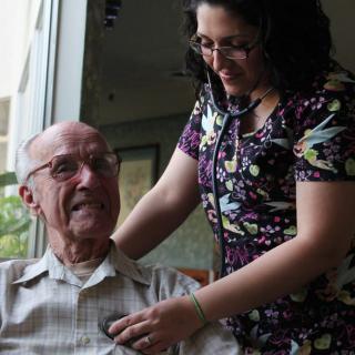 A nurse attending to an elderly patient with a stethoscope, both smiling.
