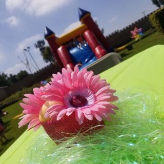 A bright outdoor party setup with a colorful flower decoration on the table and a bounce house in the background.