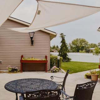 A cozy patio with metal furniture and a shade sail, overlooking a neatly manicured backyard.