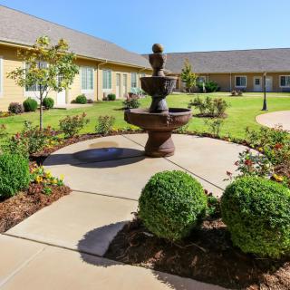 A beautifully landscaped courtyard featuring a central fountain surrounded by neatly trimmed bushes and paved walkways.
