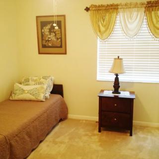 A cozy bedroom with a single bed and a nightstand beside a window adorned with curtains.