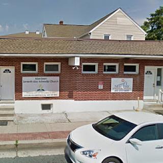 A view of a brick building featuring signage and a parked white car in front.