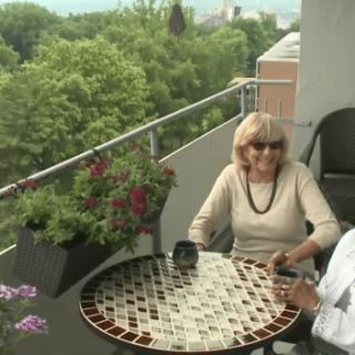 Two people sitting at a table on a balcony with plants in the background.