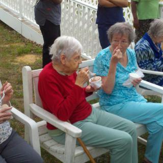 A group of elderly people sitting outside and enjoying a meal together.
