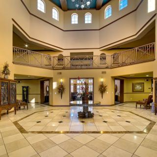 A grand lobby with a central chandelier, tiled floors, and an elegant balcony.