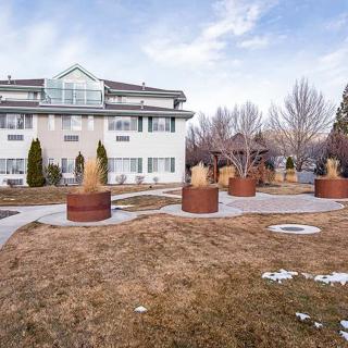 An apartment building with landscaped grounds, featuring large potted plants and bare trees under a cloudy winter sky.