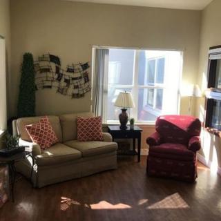 A cozy living room with a sofa, armchair, and ample natural light streaming through a large window.