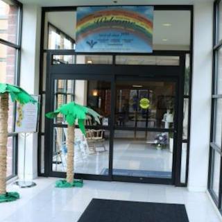 Entrance with decorative palm trees and welcoming sign overhead.