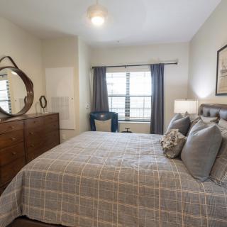 A cozy and well-decorated bedroom featuring a comfortable bed, a dresser with a mirror, and curtains framing the window.