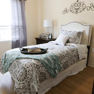 A cozy and stylish bedroom with a single bed featuring patterned bedding, a bedside lamp, and decorative details.