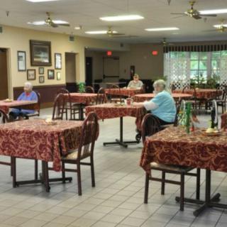 A quiet dining area with a few people seated at tables, likely in a community or retirement home setting.
