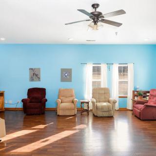 A spacious living room with blue walls, featuring comfortable chairs, wooden flooring, and a ceiling fan.