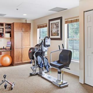 A well-lit home gym featuring a stationary bike and exercise equipment.