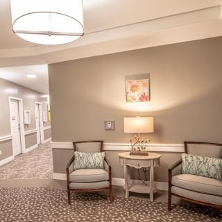 A cozy lobby with a seating area, featuring two chairs and a lamp on a side table.