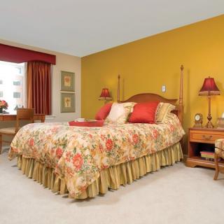 A cozy traditional bedroom featuring a colorful floral bedspread, warm yellow accent wall, and matching lamps.