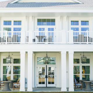 A white two-story house with large windows and a balcony.