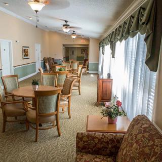 A well-lit, comfortable seating area with tables and chairs, featuring large windows and elegant drapes.