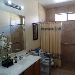 A well-lit bathroom featuring a large mirror, sink, handrails for accessibility, and a shower with a curtain.