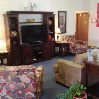 A cozy living room with a TV stand, floral chairs, sofa, and decorative elements.