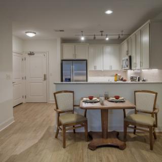 A modern kitchen with a small dining table and chairs, featuring appliances and a minimalist design.