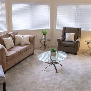 A cozy living room with a sofa, armchair, and glass coffee table, featuring neutral colors and decor.