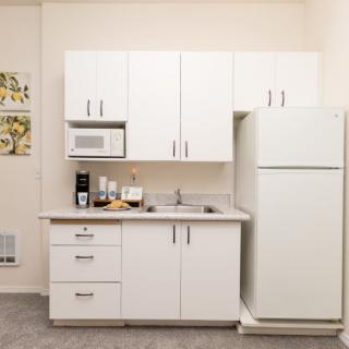 A compact kitchen setup featuring white cabinets, a refrigerator, microwave, and a sink.