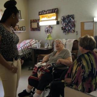 A caregiver interacts with two seniors in a nursing home setting.
