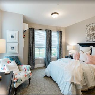 A cozy and well-decorated bedroom with a bed, armchair, lamps, and large windows.