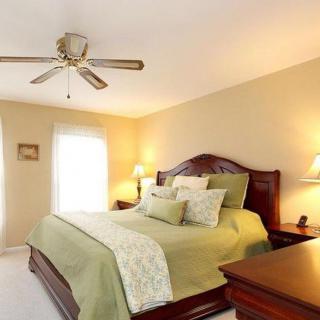 A cozy bedroom with a large bed, ceiling fan, and warm lighting.