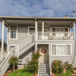 A two-story residential house with a porch and stairs leading to the entrance, surrounded by a small front yard.