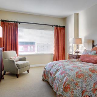 A cozy bedroom featuring a colorful bedspread, an armchair, and red curtains.