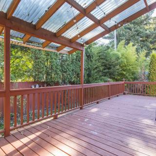 A spacious wooden deck with a pergola roof, overlooking a lush garden.