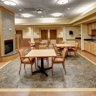 A welcoming community room with tables and chairs, featuring a cozy fireplace and kitchenette.