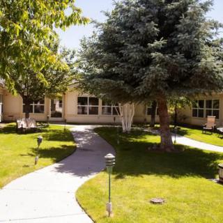 A scenic garden pathway leading to a residential building surrounded by lush trees and a well-maintained lawn.