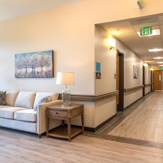 A well-lit hallway featuring a cozy lounge area with a sofa, lamp, and contemporary artwork.