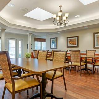 A well-lit dining room featuring wooden tables and chairs, decorative paintings, and a chandelier.