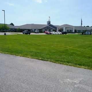 A view of a building surrounded by grassy areas and parked vehicles under a clear sky.