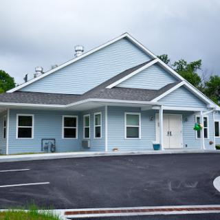 A modern blue building with a sloped roof, surrounded by a well-maintained parking area and an overcast sky.