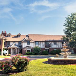 A picturesque building with Tudor-style architecture featuring a central fountain and well-maintained landscaping on a sunny day.