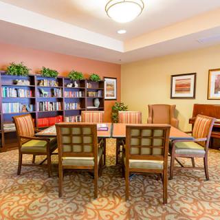A cozy reading room with a central table surrounded by chairs and bookshelves.
