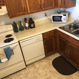 A cozy kitchen with wooden cabinets featuring a stove, microwave, dishwasher, and various decorative items on the countertop.