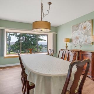 A spacious dining room with a long table, surrounded by wooden chairs, and a large window offering a scenic view.